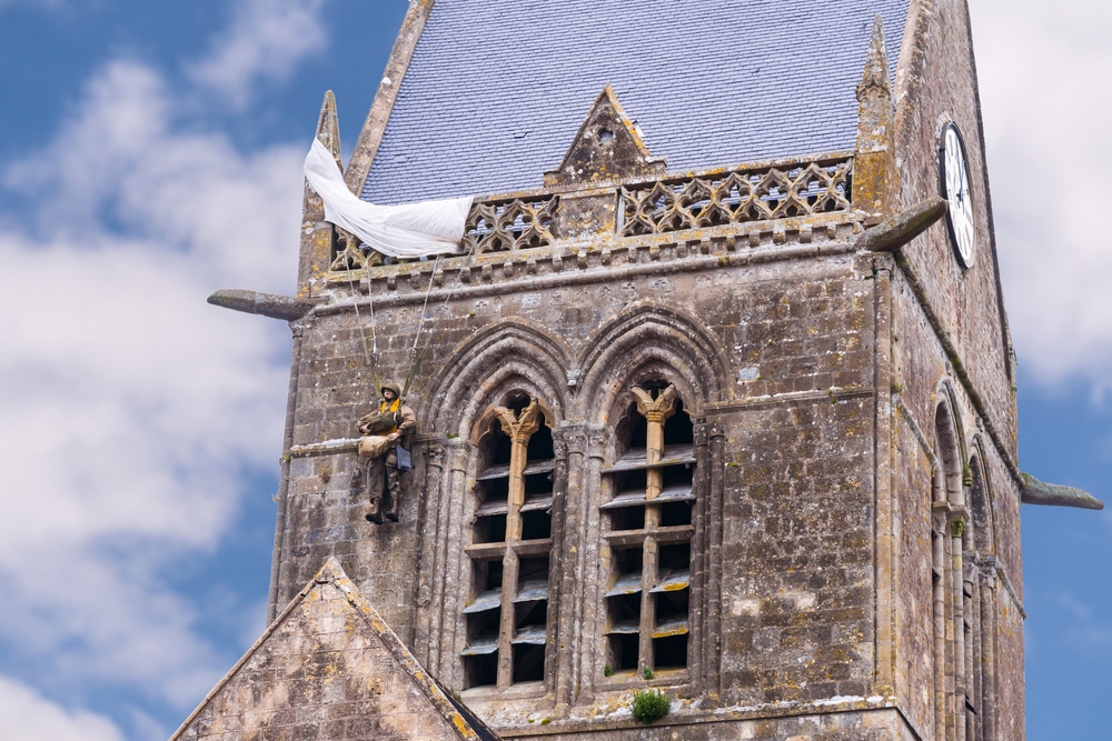 De klokkentoren van de kerk van Saint-Mère-Église waar een beeld van een parachutist aan hangt.
