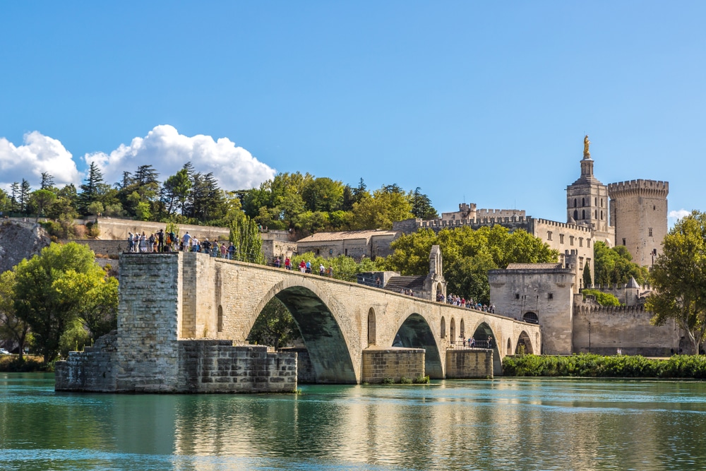 Stenen gebouwen en stenen brug van Avignon over het water en omringd door groene bomen.