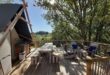 terras van een safaritent met tuinmeubilair en een buitenkeuken en uitzicht op een groene heuvel op Camping Les Arches in de Ardèche