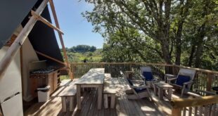 terras van een safaritent met tuinmeubilair en een buitenkeuken en uitzicht op een groene heuvel op Camping Les Arches in de Ardèche