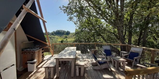 terras van een safaritent met tuinmeubilair en een buitenkeuken en uitzicht op een groene heuvel op Camping Les Arches in de Ardèche