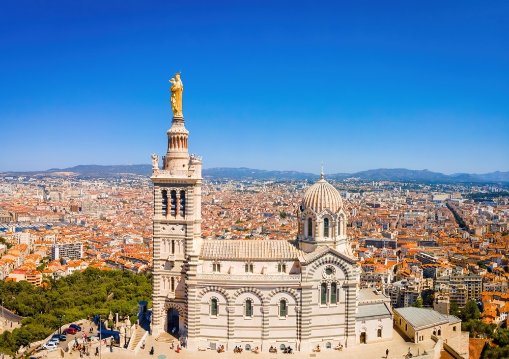 Bijzondere witte basiliek met gouden standbeeld dat uittorent boven de rest van de stad. Uitzicht op de oranje daken van de huisjes in Marseille.