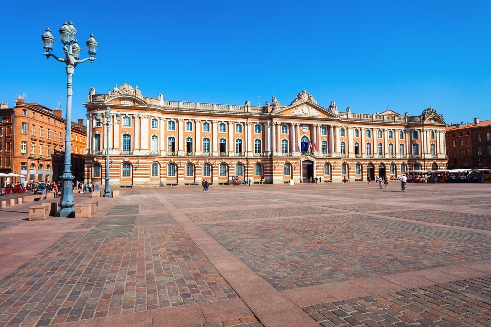 het plein Place du Capitole met enkele mensen, het stadhuis en markt aan de zijkant van het plein op en zonnige dag