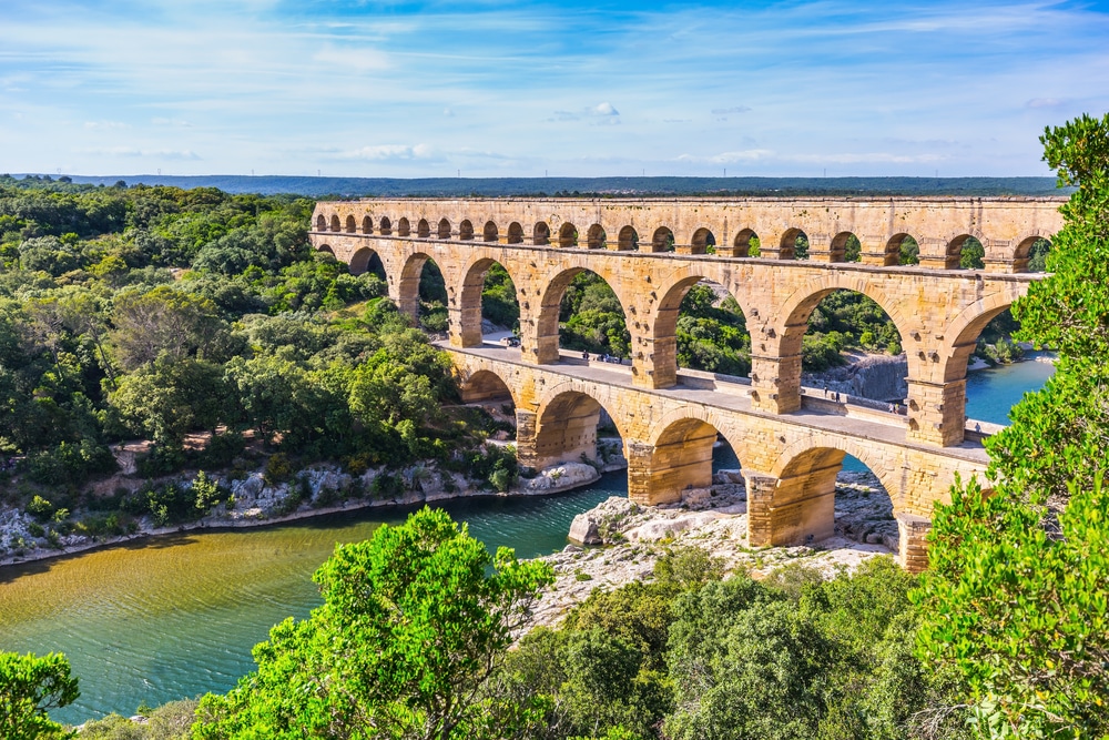 Hoge, stenen aquaduct over rivier de Gardon en omringd door groene bomen.