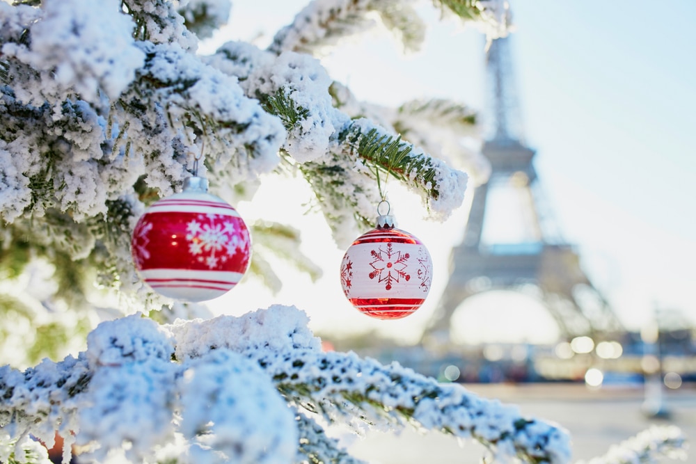 twee kerstballen in een besneeuwde kerstboom met op de achtergrond de Eiffeltoren