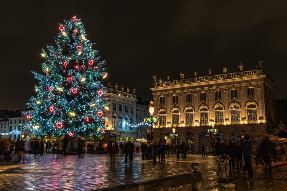 kerstboom met verlichte hartjes en verlichte flitsen, en verlichte gebouwen op een plein in Nancy