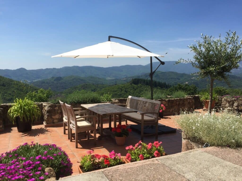 terras van een vakantiehuis in de Ardèche met een tuintafel en daaraan een houten bankje en twee stoelen onder een parasol