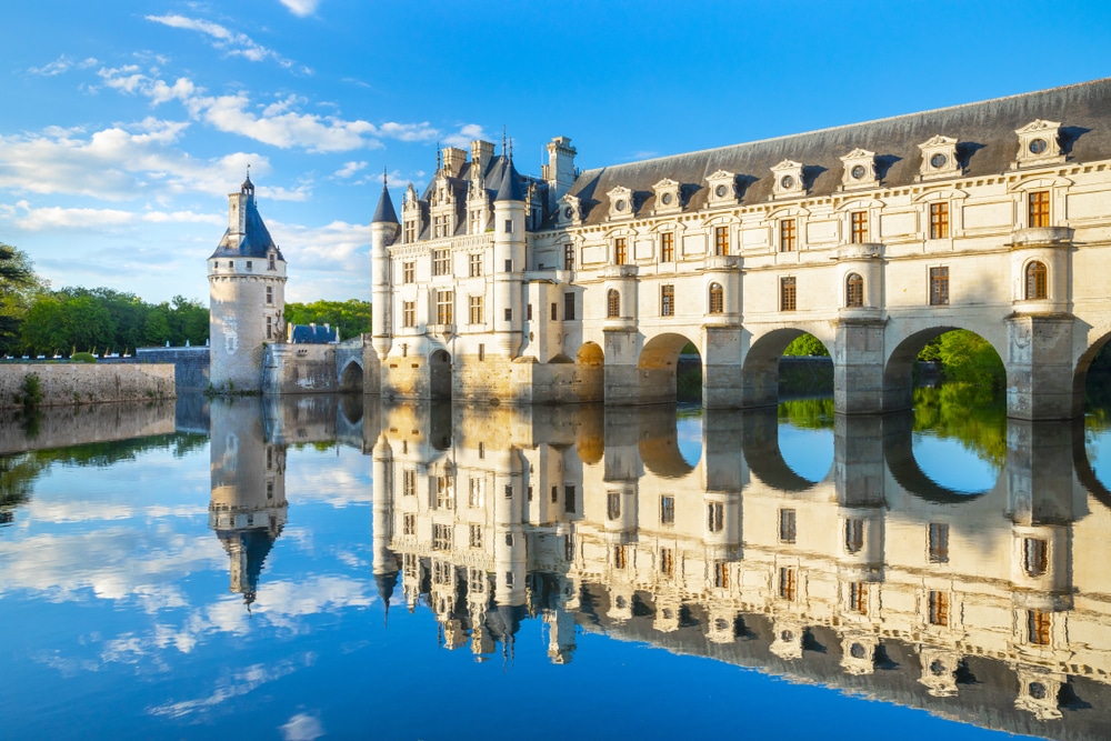 Groot wit kasteel met zwarte daken en bogen aan de onderkant gelegen over rivier de Loire heen.