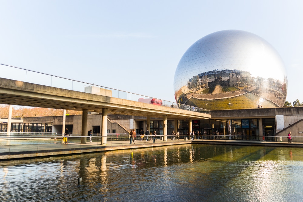 Modern rond gebouw met spiegels gebouwd op een stenen brug en gelegen aan het water.