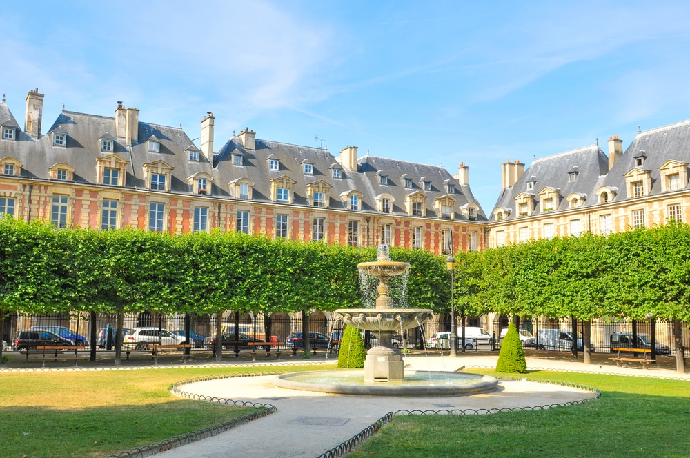 Het plein Place des Vosges met een fontein in het midden en omringd door groene bomen en huizen.