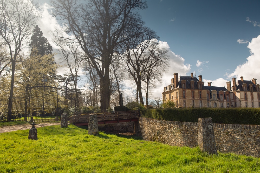 Groen park met bomen en stenen bruggetje met daar rechts van het kasteel van Thoiry.