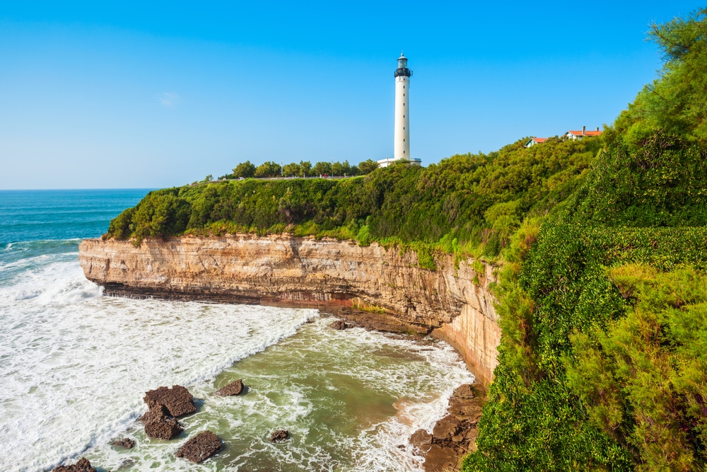 Witte vuurtoren van Biarritz gelegen op een rots met groene bossen grenzend aan de Atlantische oceaan.
