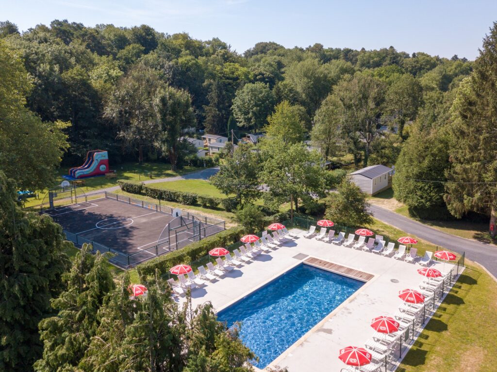 luchtfoto van Camping le Grand Paris met een foto van het lege zwembad, sportveld en enkele stacaravans tussen de bomen