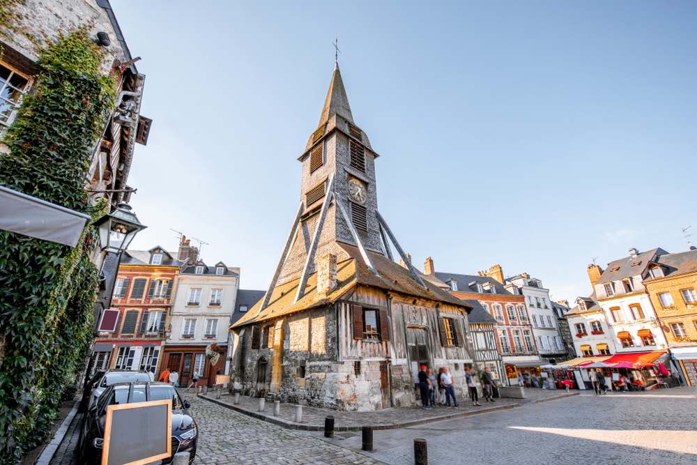 Het plein Place Sainte-Catherine in Honfleur met de puntige Sainte-Catherinekerk in het midden en omringd door kleurrijke pittoreske huisjes.