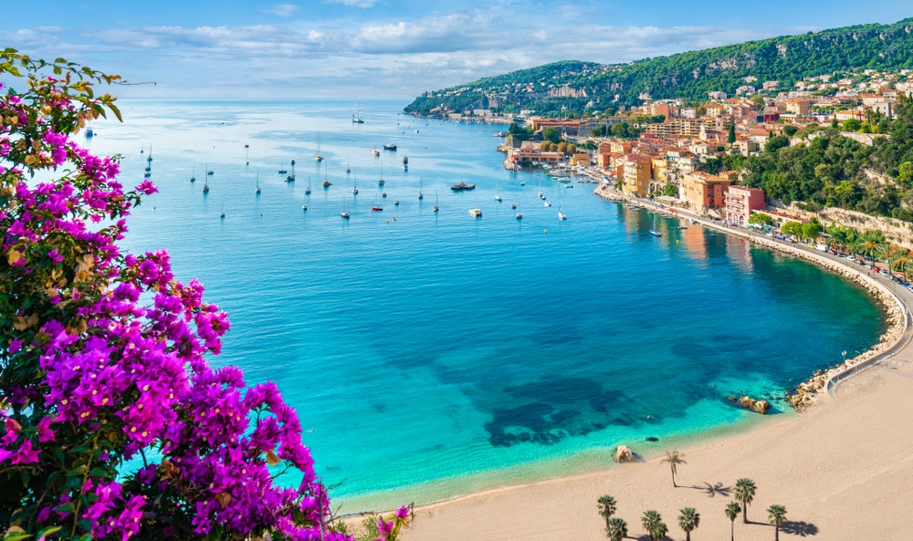 azuurblauwe baai met een leeg strand en verderop in de zee bootjes in Nice
