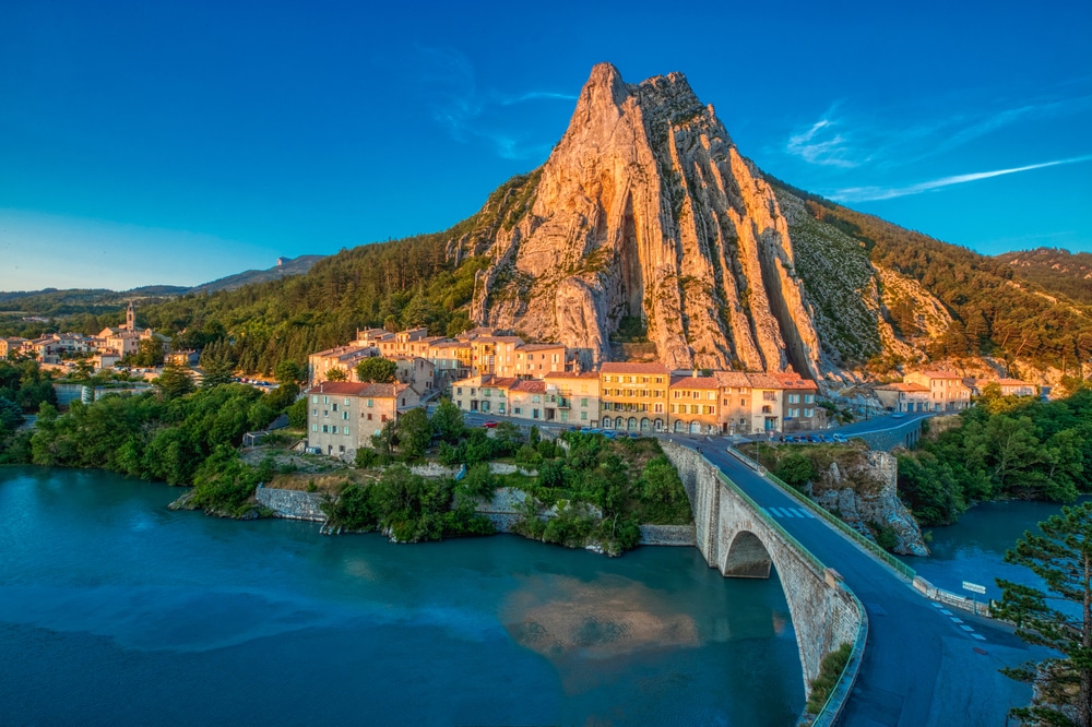 Toegangsweg naar het dorp Sisteron, liggend aan de oever van een rivier onder de hoge rotswand Rocher de la Baume.