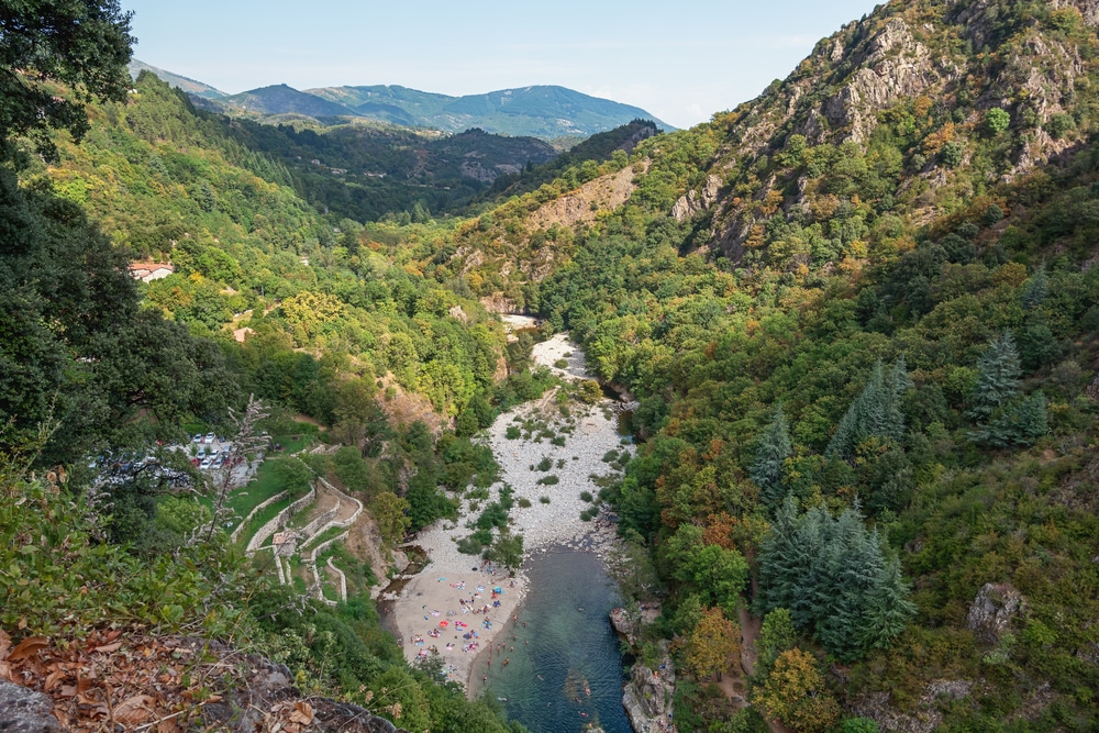 Een inham van rivier de Ardèche met een klein strand gelegen tussen grote, begroeide rotsen.