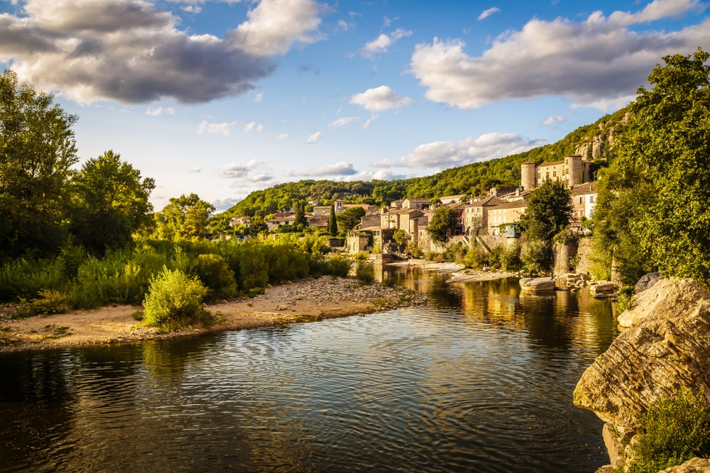 Goudkleurig kalkstenen huisjes gelegen boven rivier de Ardèche en omringd door groene bossen en bomen.