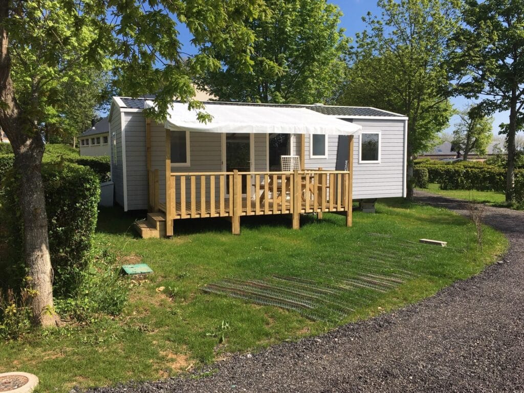 grijze stacaravan met een houten vlonder met houten picknicktafel en een witte overkapping op Caming Abijune