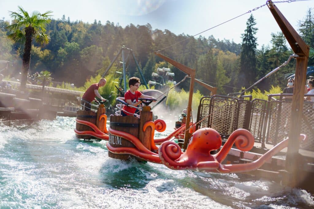 foto van een man en een jongetjes beide in een eigen karretje met stuur boven het water in attractiepark Fraispertuis City