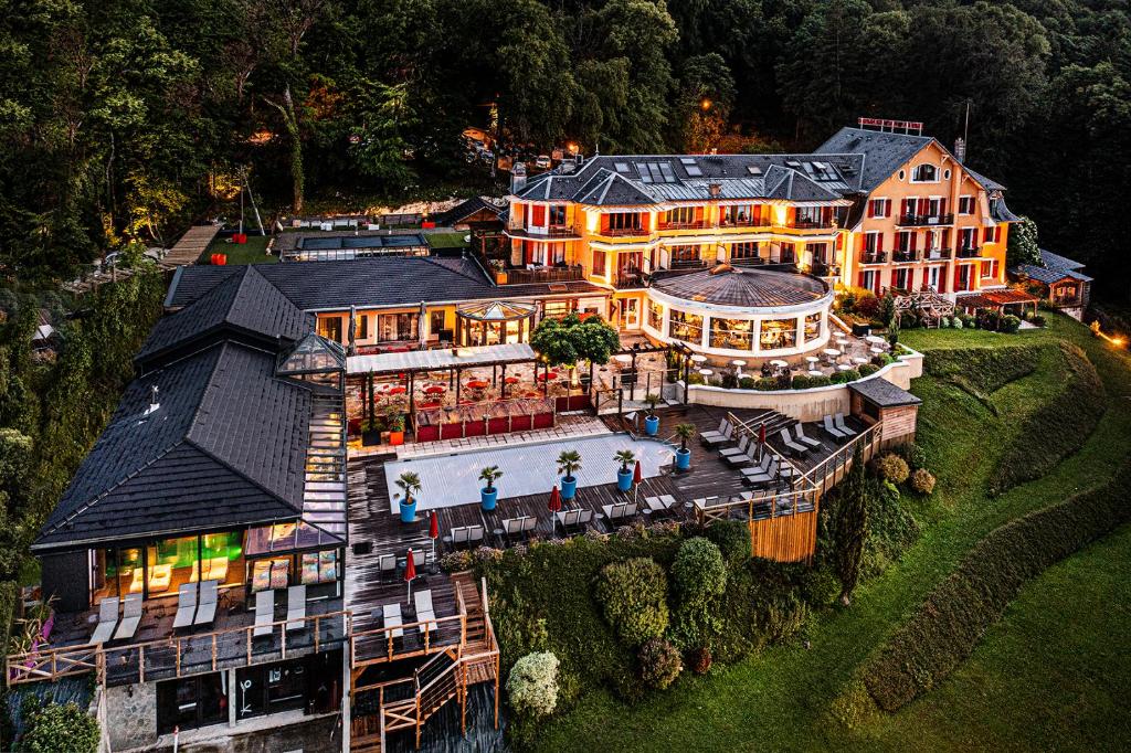 Groot hotel resort met verschillende kamers, een zwembad, ligstoelen en een zwart dak gelegen tussen groene bomen en bossen.