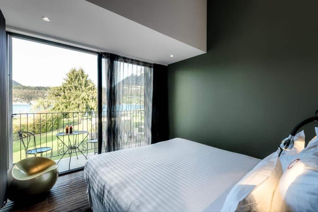 hotelkamer met donkergroene muur, een wit bed en balkon met tuinset en uitzicht op het meer van Annecy